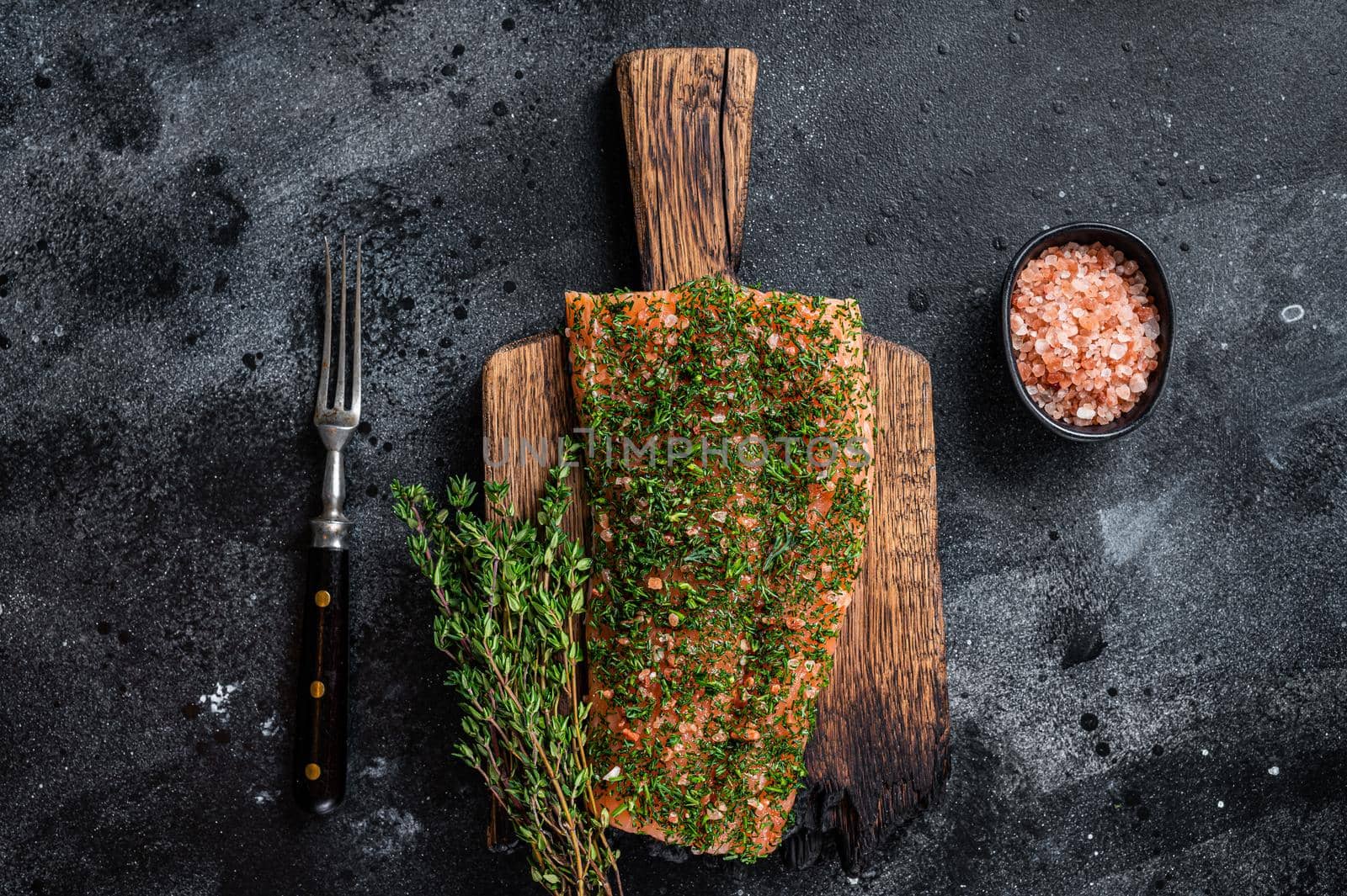 Gravlax cured salmon with dill and salt on wooden board. Black background. Top view.