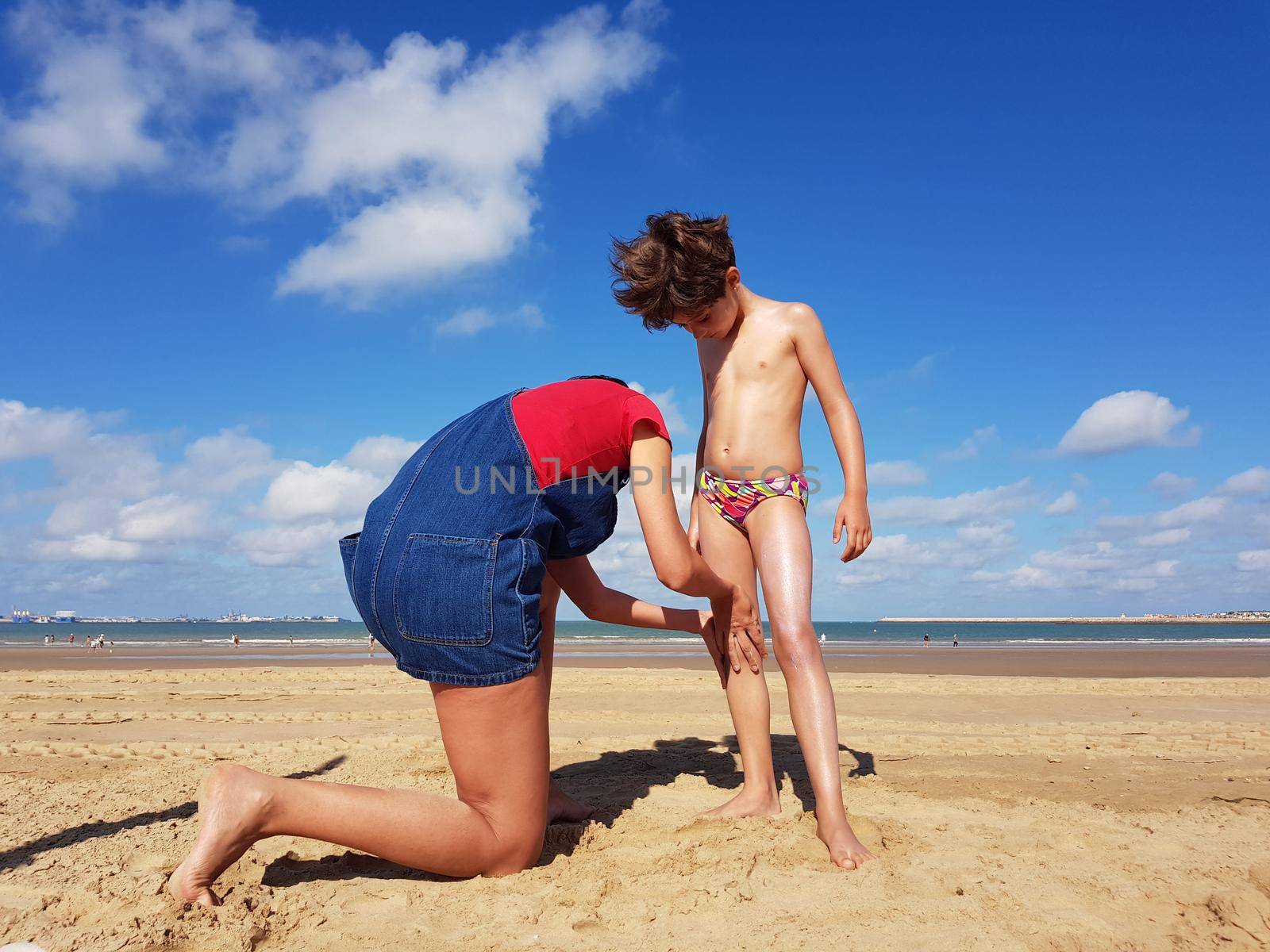 Mother throwing sunscreen on her little daughter on a tropical beach