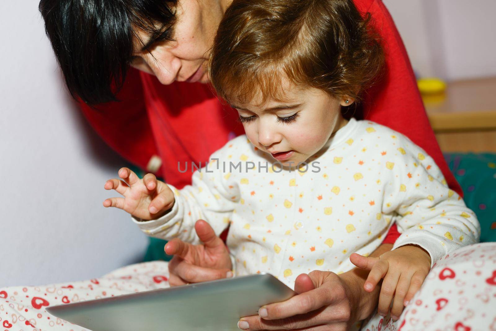 Mother reading bedtime stories to her little daughter on digital tablet