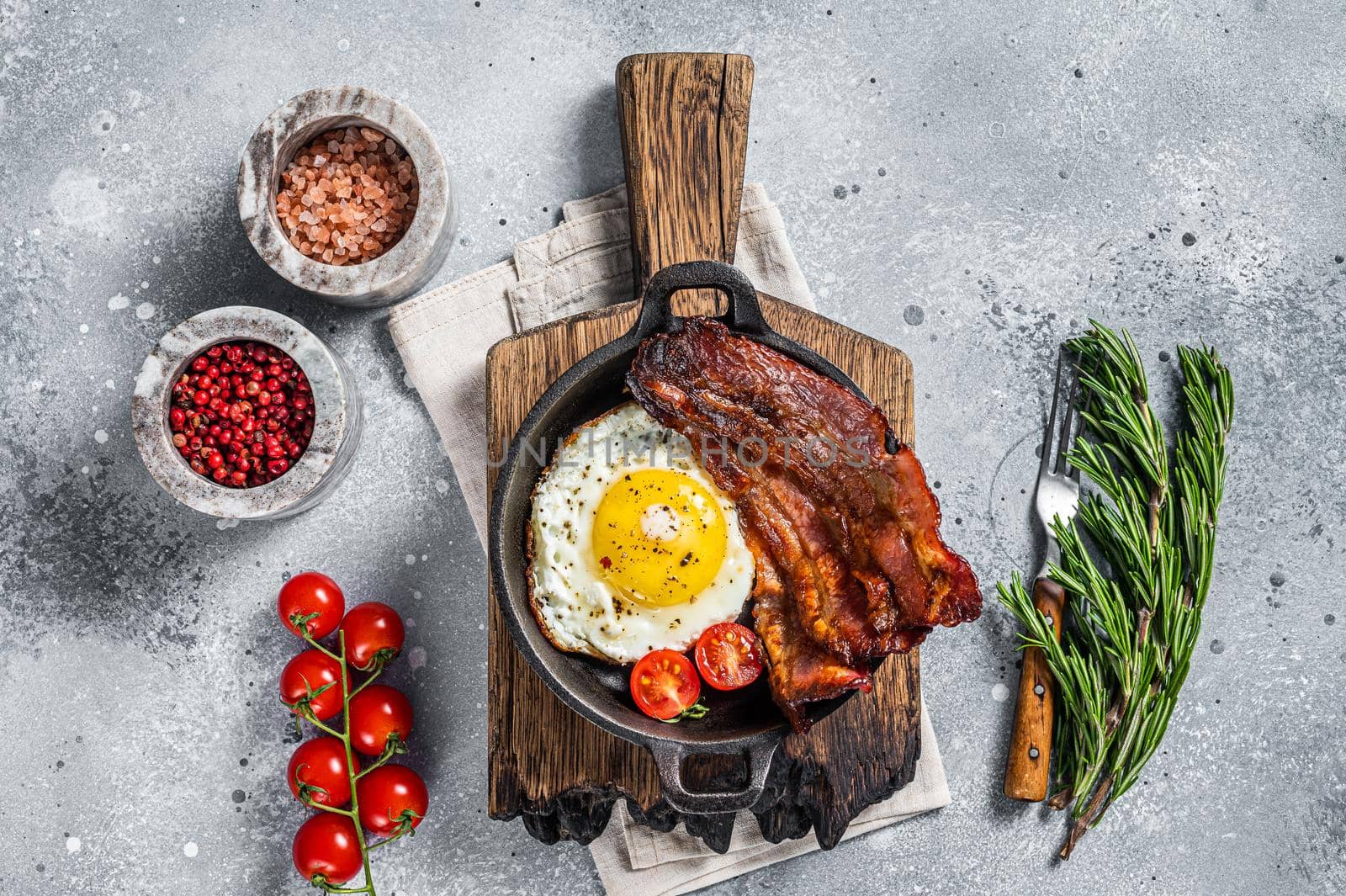 English breakfast with fried egg and bacon in cast iron pan. Gray background. Top view.