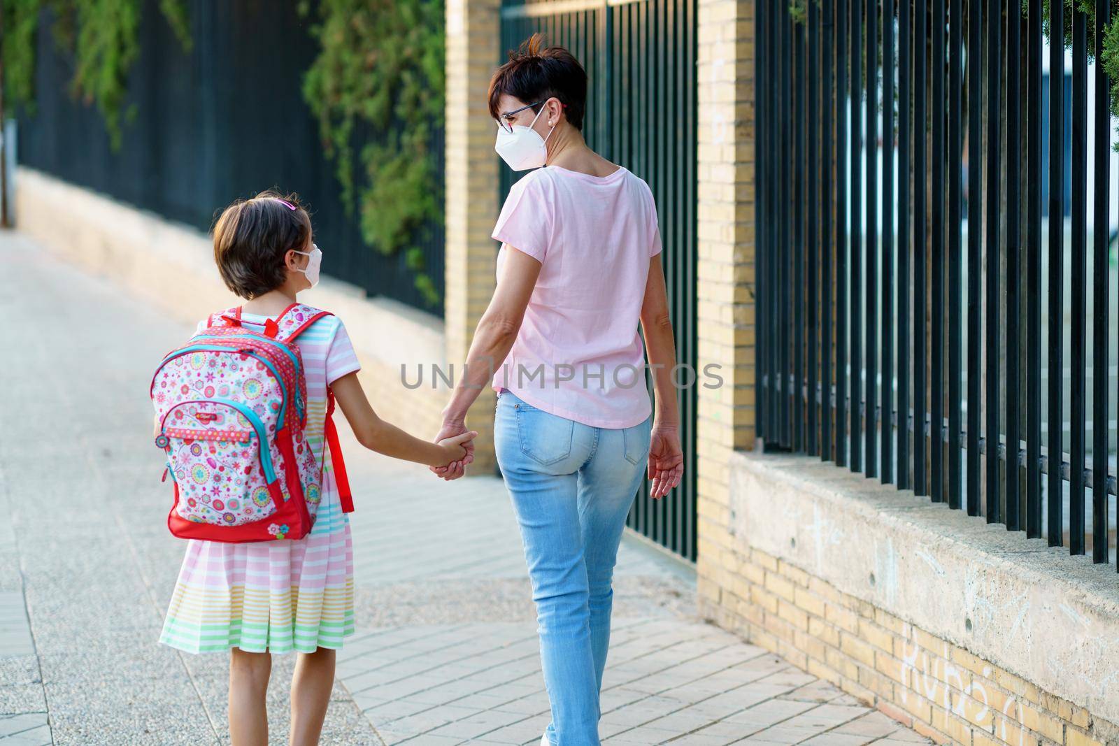 Nine years old girl with bag walking with her mother hand in hand. by javiindy