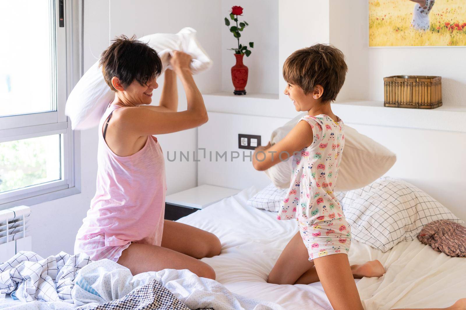 Mother and daughter having funny pillow fight on bed. by javiindy