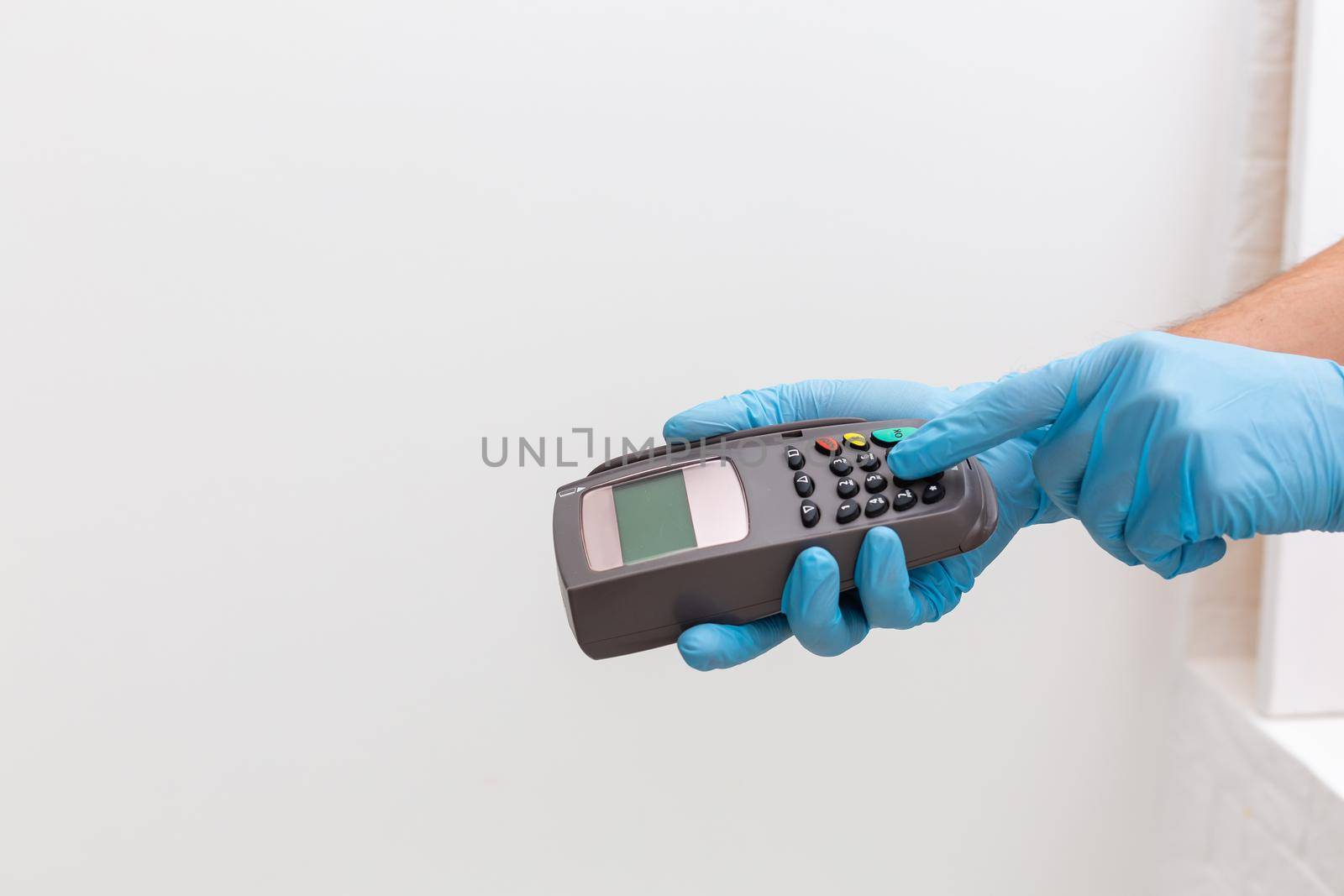 Cashier hand holding credit card reader machine and wearing disposable gloves, paying with smartphone during Covid-19 pandemic.