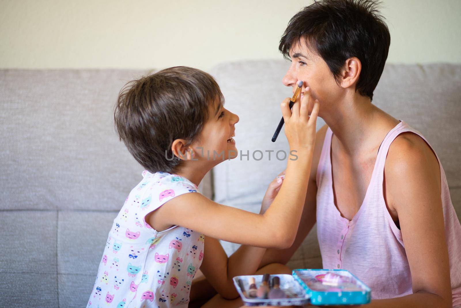 Happy beautiful mother and her little cute daughter doing make up for each other. Mum spending free time with her daughter.