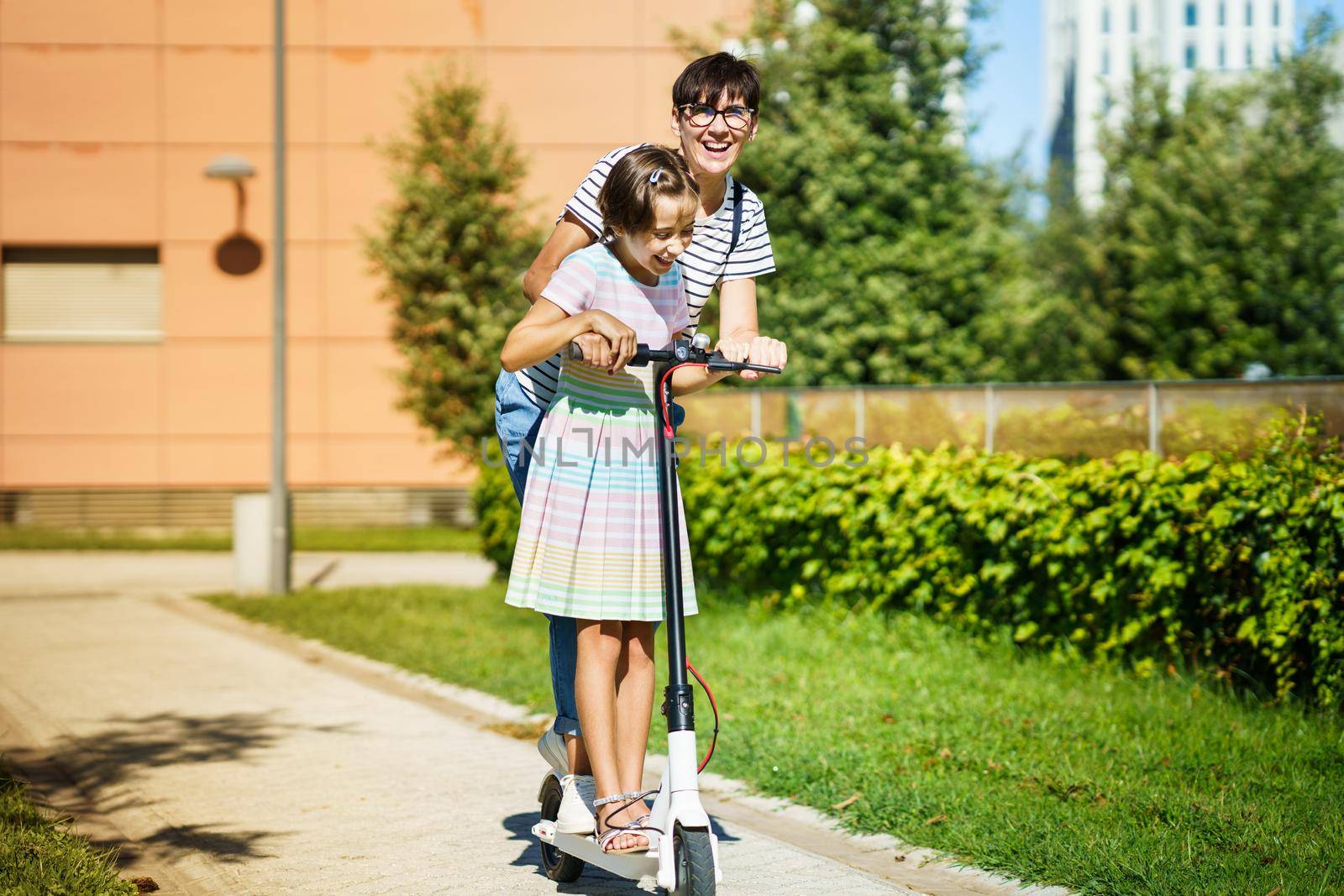 Mother and daughter riding on electric scooter in the city street.