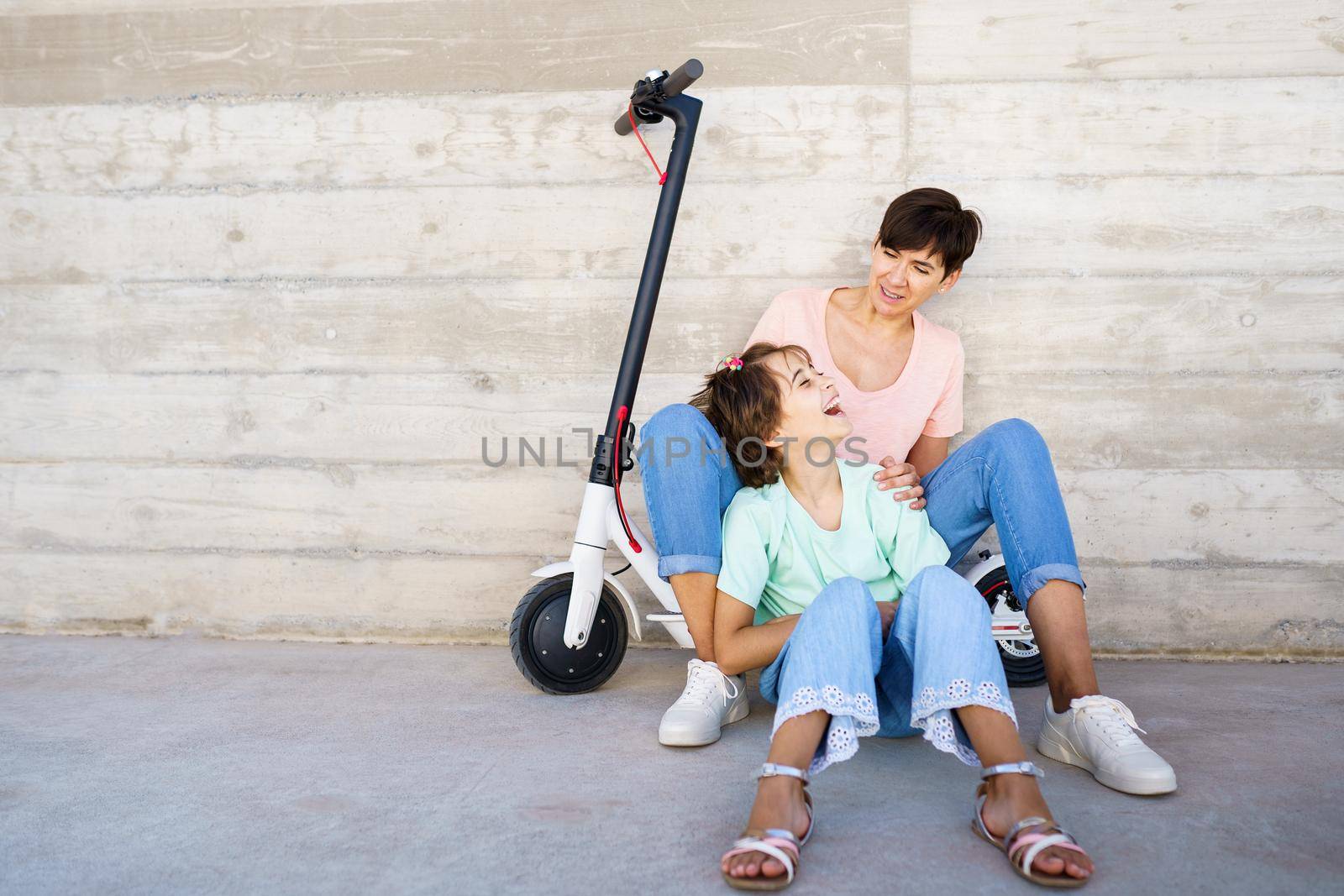 Mother and daughter laughing sitting on an electric scooter in the city street