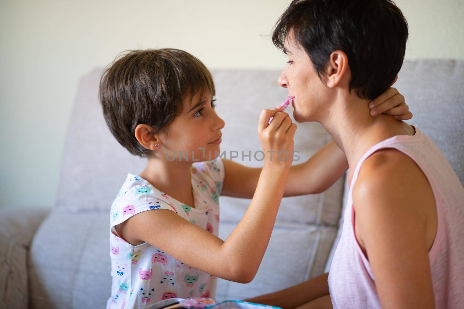 Happy beautiful mother and her little cute daughter doing make up for each other. Mum spending free time with her daughter.