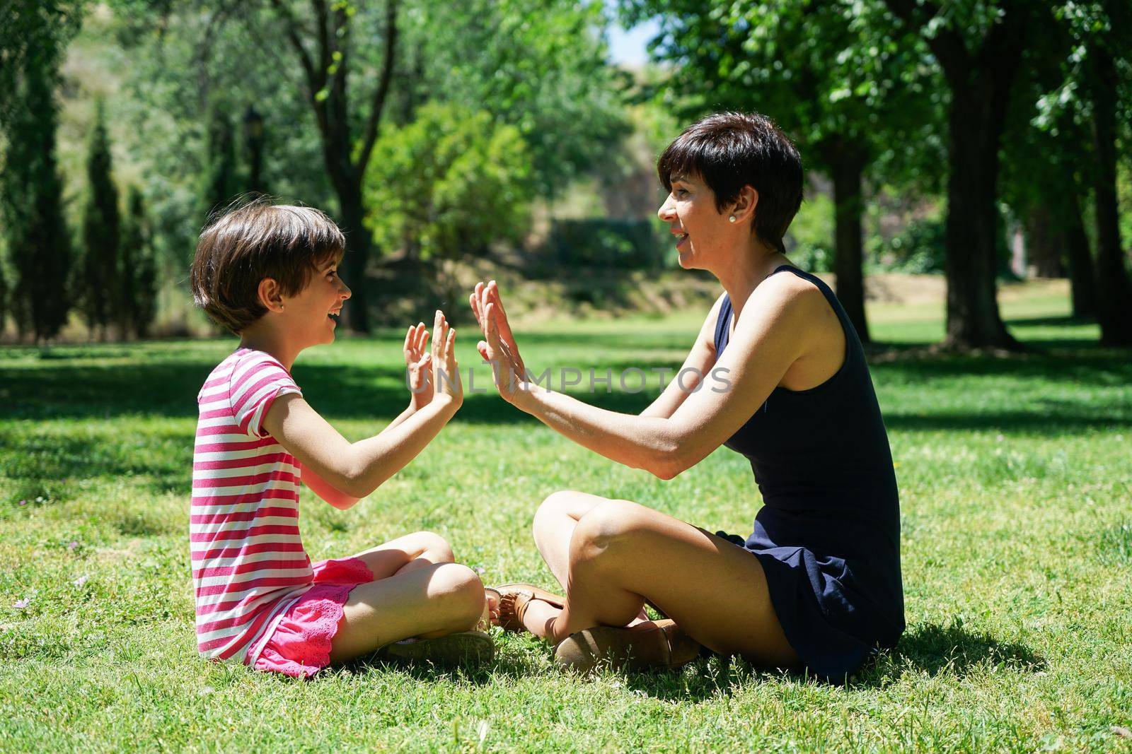 Mother and daughter playing with hands in city park. Happy loving family.