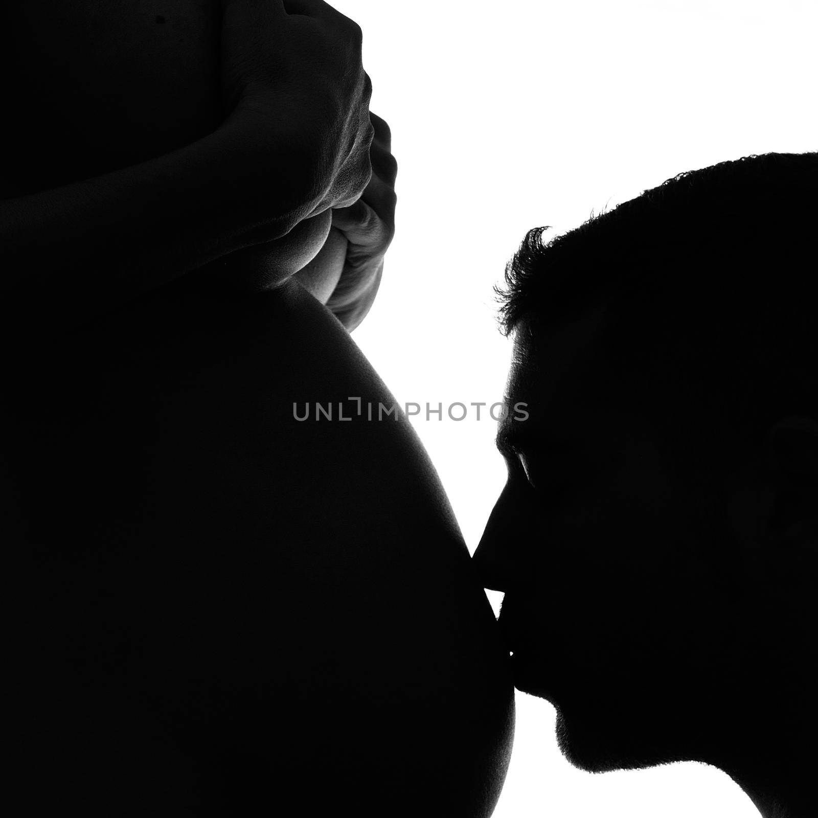 Man kissing his pregnant wife's belly in black and white