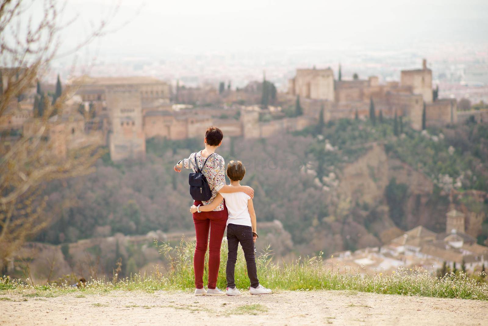 Mother and little daughter looking at the Alhambra of Granada from Cerro de San Miguel. Single parent family doing tourism.