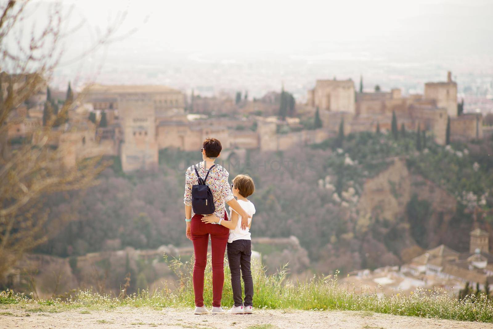 Mother and little daughter looking at the Alhambra of Granada from Cerro de San Miguel. Single parent family doing tourism.