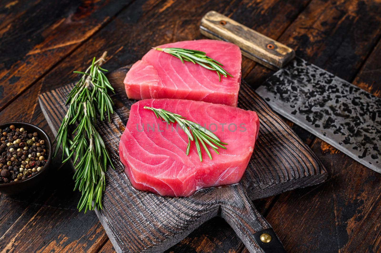 Raw tuna steaks on a wooden cutting Board with cleaver. Dark wooden background. Top view by Composter