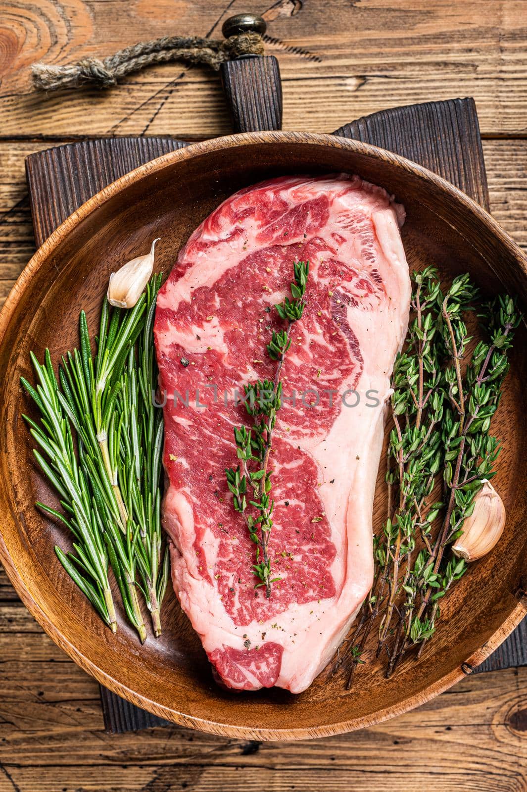 Fresh new york strip beef meat steak or striploin in a wooden plate with herbs. wooden background. Top view.