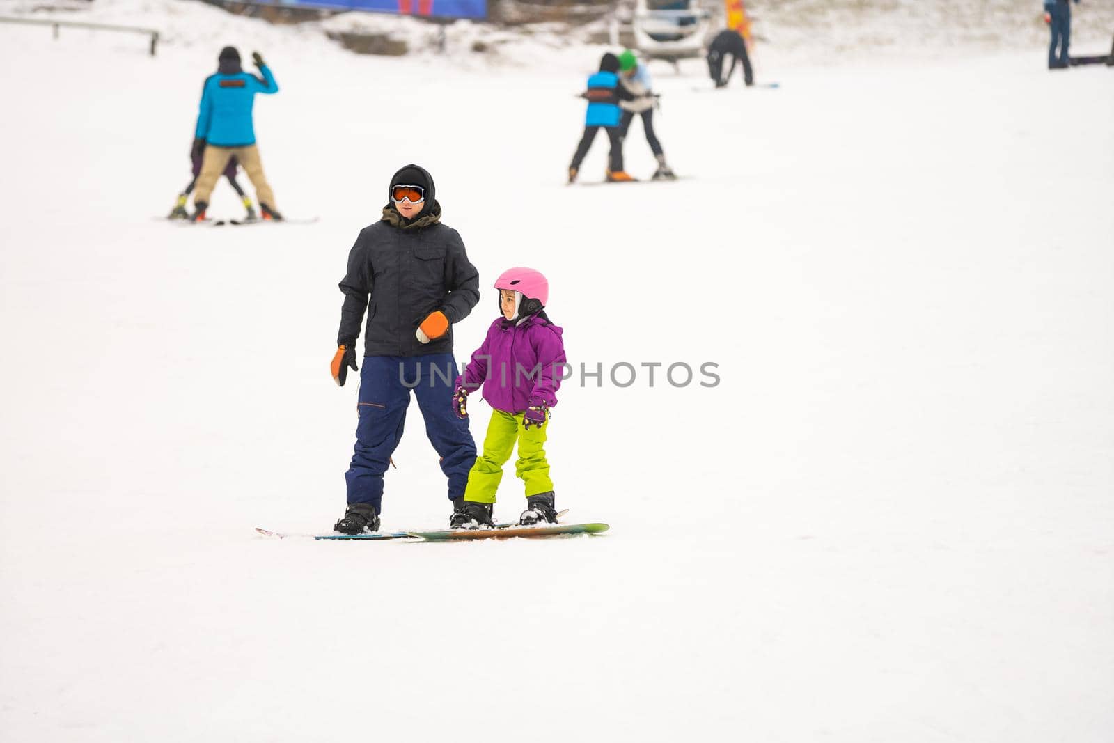 Instructors teach a child on a snow slope to snowboard