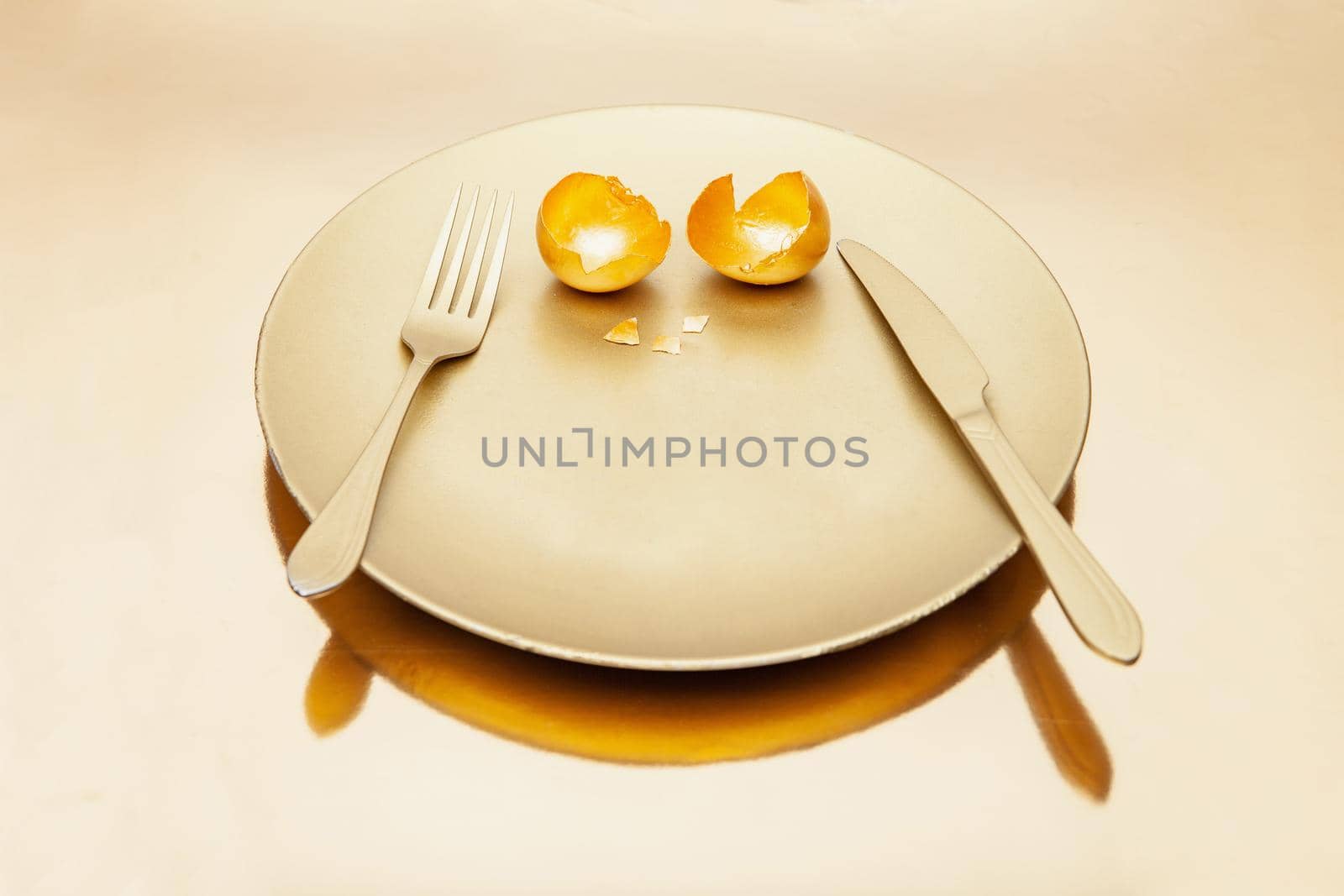 Cutlery and golden eggshell on plate placed on reflective table by Julenochek