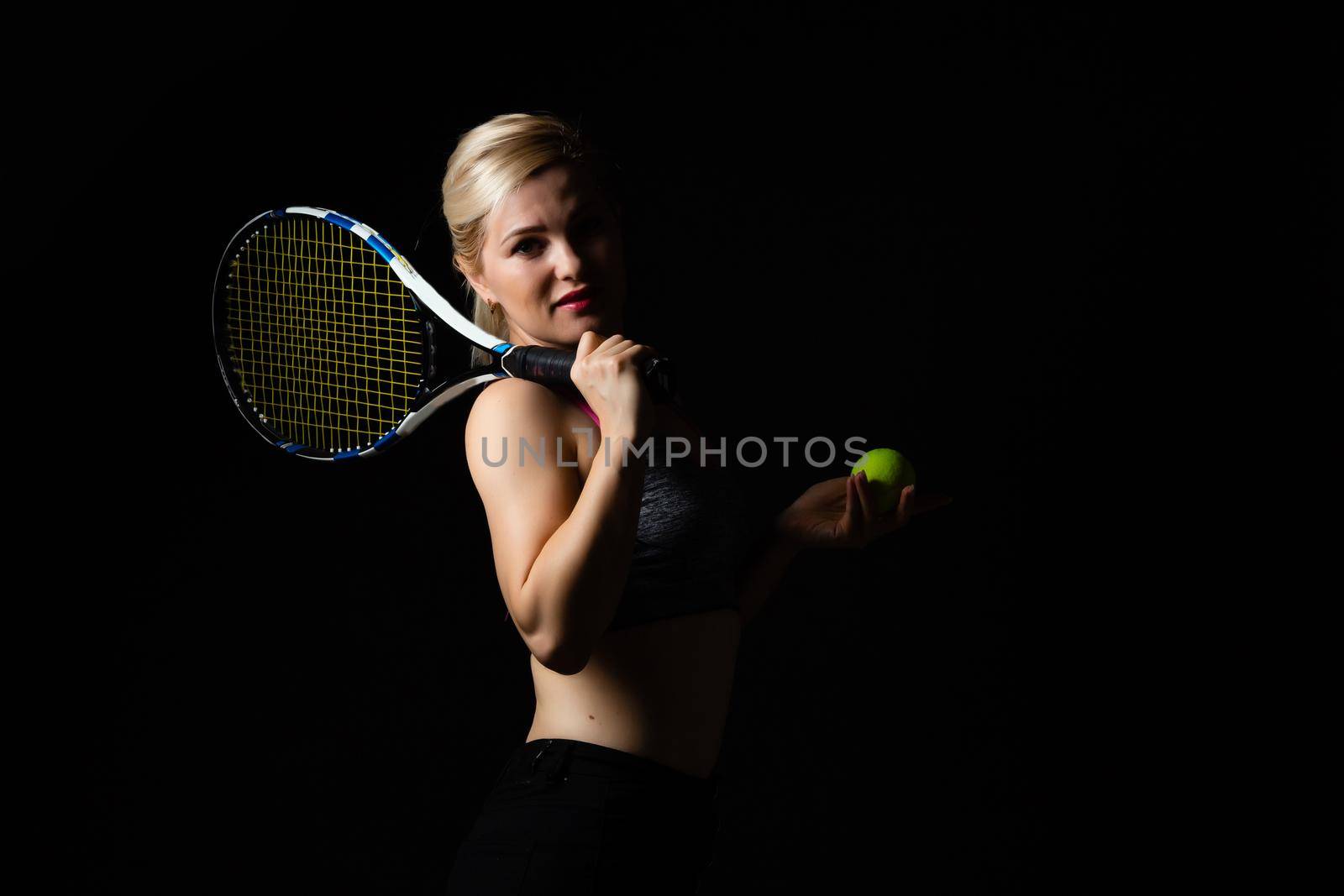 Female tennis player with racket and ball on black background