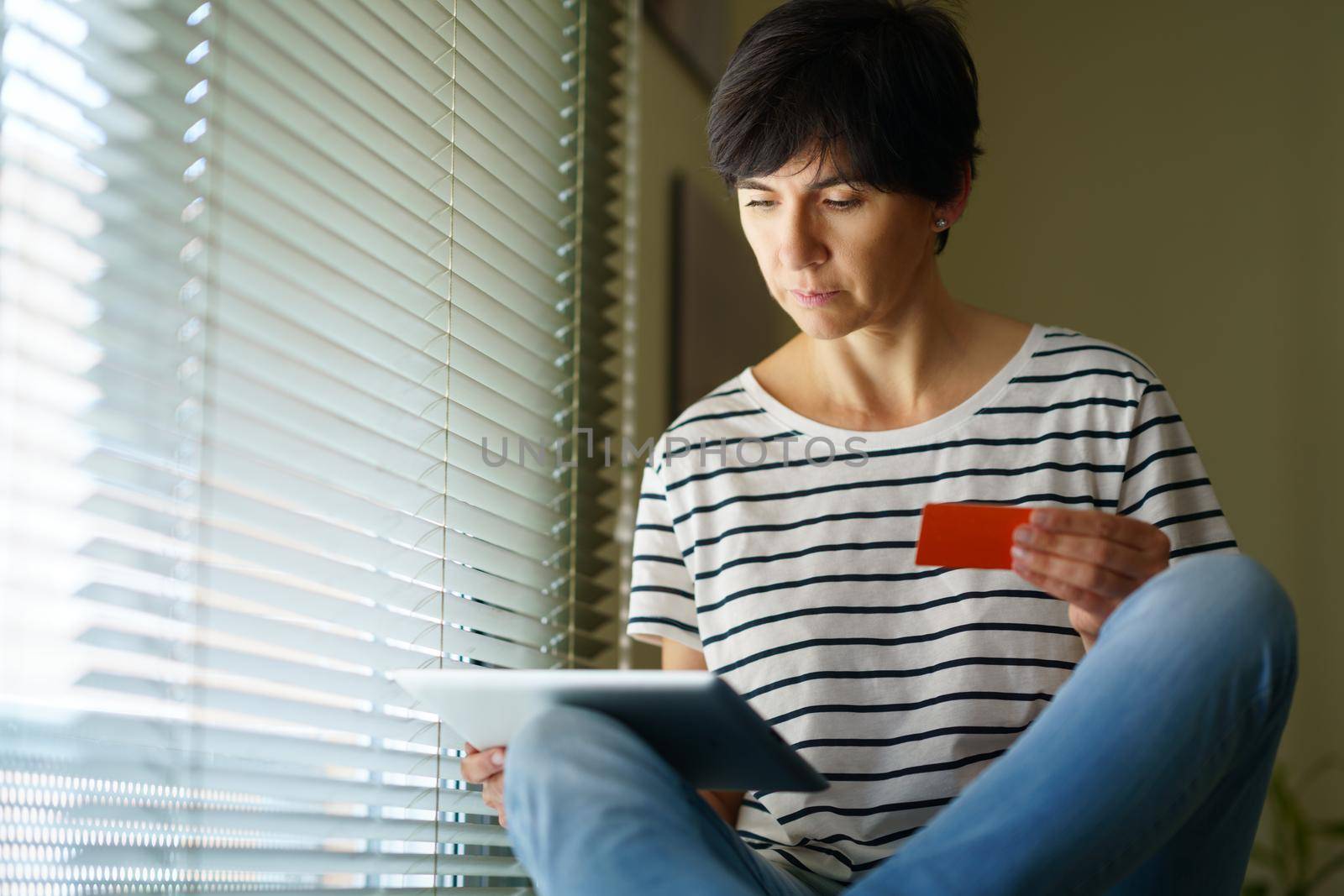 Middle-aged woman shopping online with her digital tablet paying with a credit card. Female in her 50s