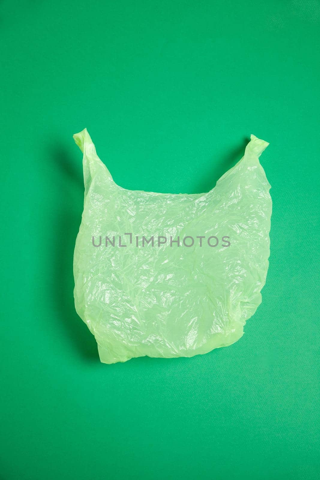 Top view of crumpled simple plastic bag placed on bright green background in studio