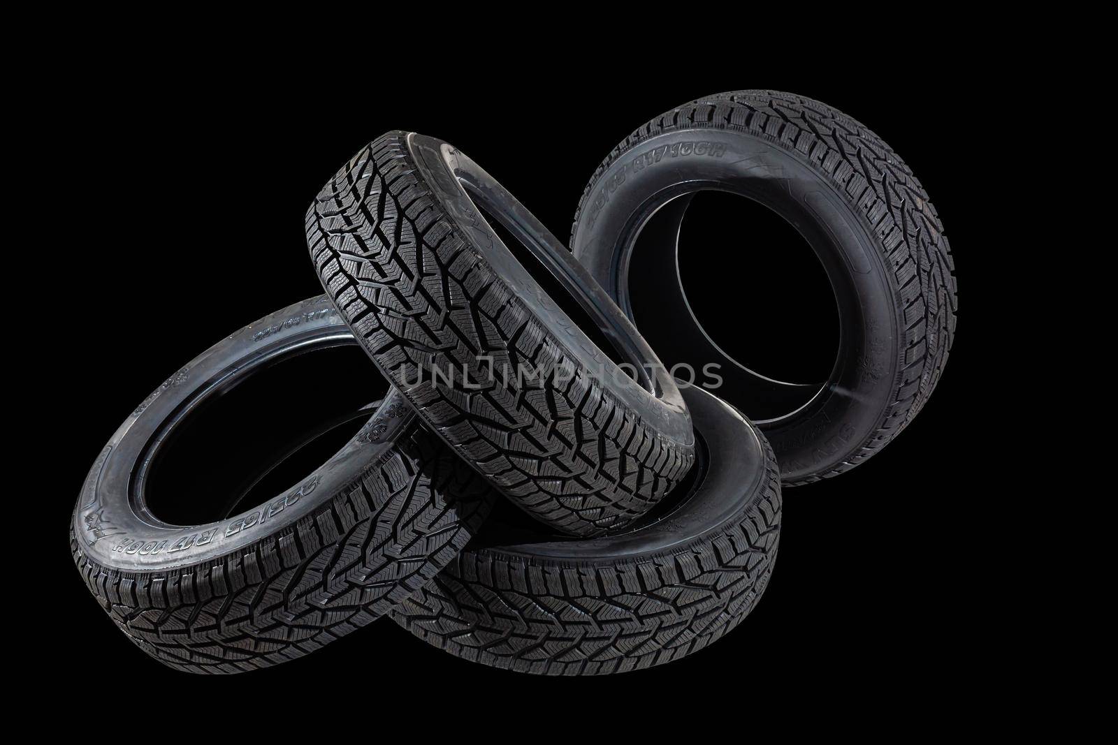 Stack of four new black tyres for winter car on black background by Andelov13