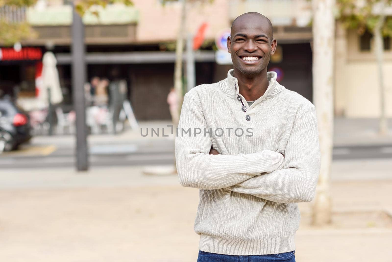 Black young man with arms crossed smiling in urban background by javiindy