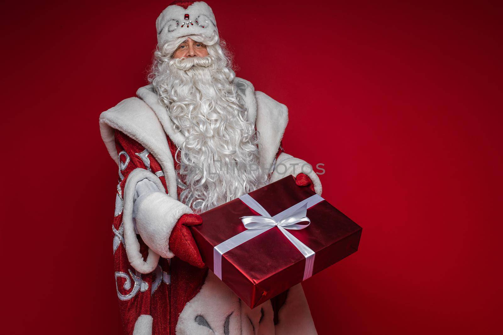 Stock photo of smiling happy Santa in traditional hat with rhinestones and long white beard looking at camera. Cutout on red background. Happiness concept.