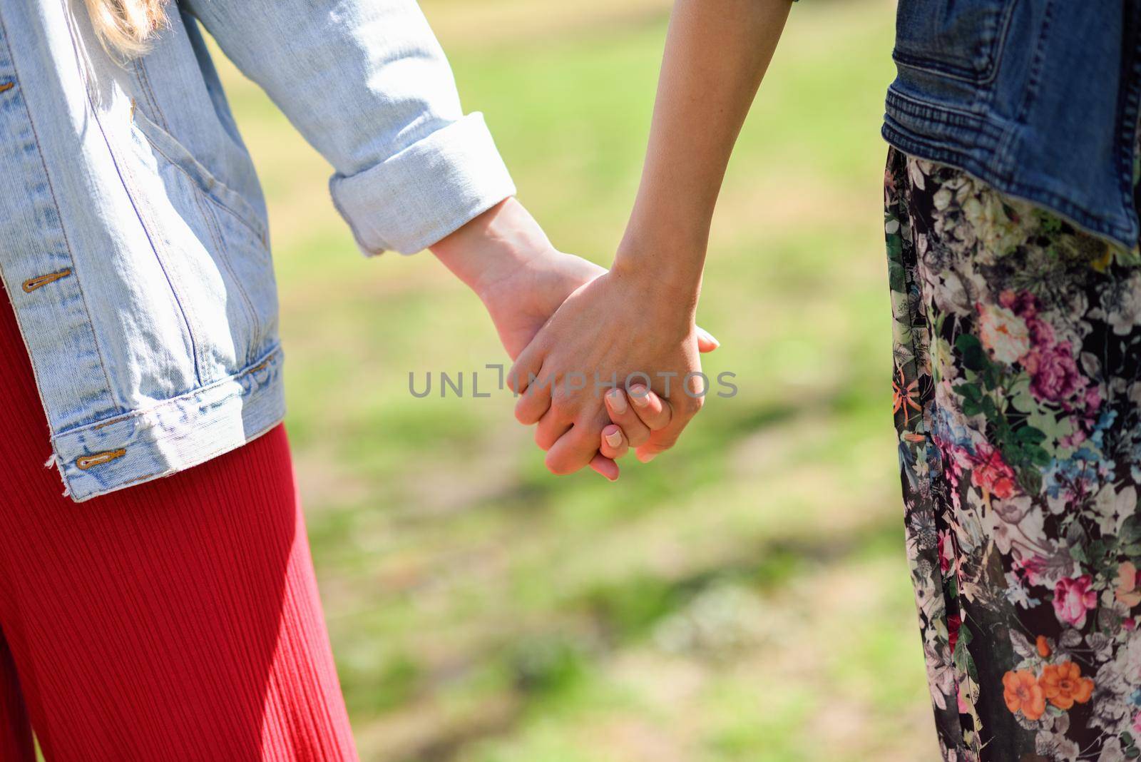 Two young women in walking holding her hands in urban park. by javiindy