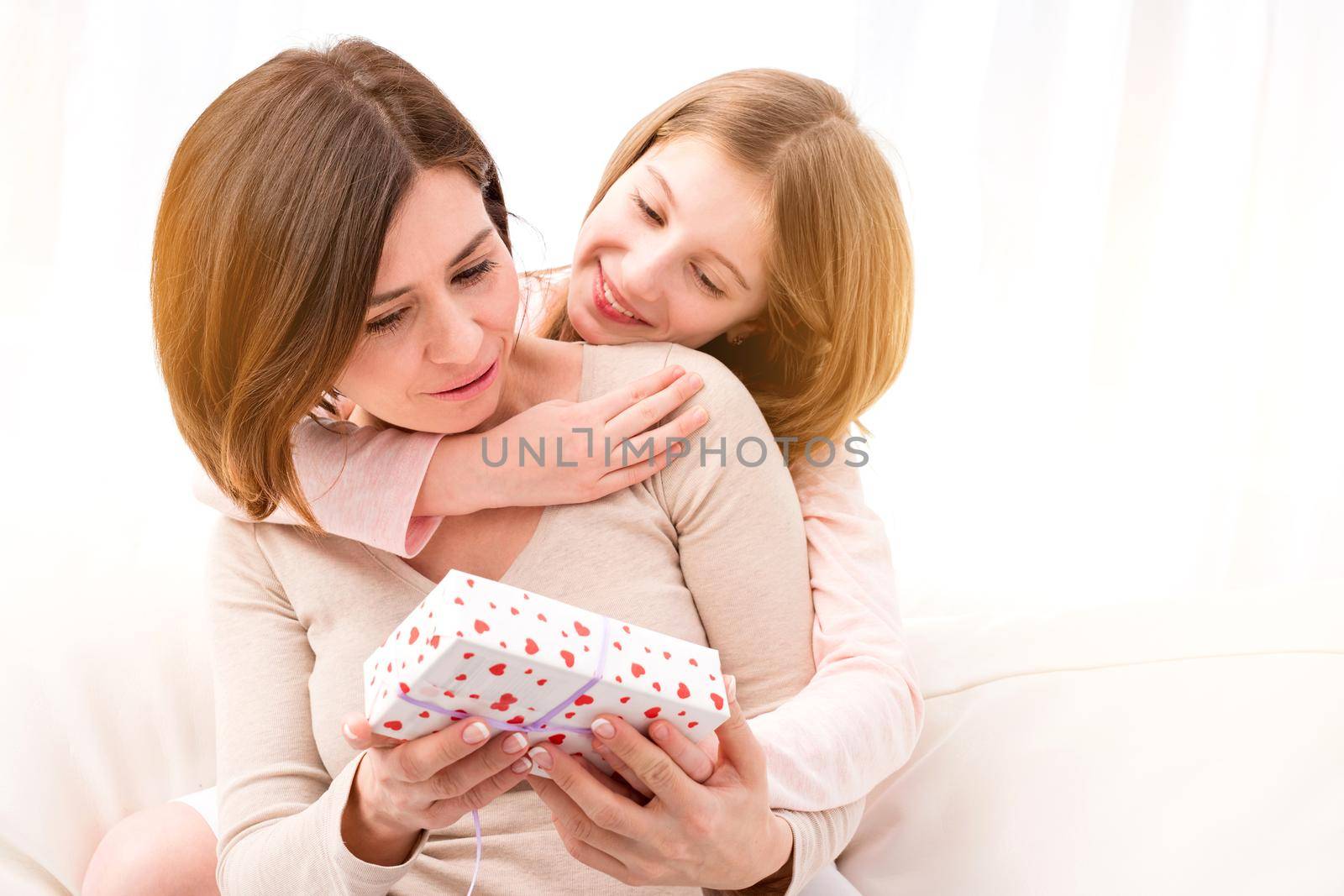 Happy Mother's Day, happy woman's day, happy birthday. Beautiful little girl giving her mother small wrapped gift box. Daughter embracing and congratulating her mum