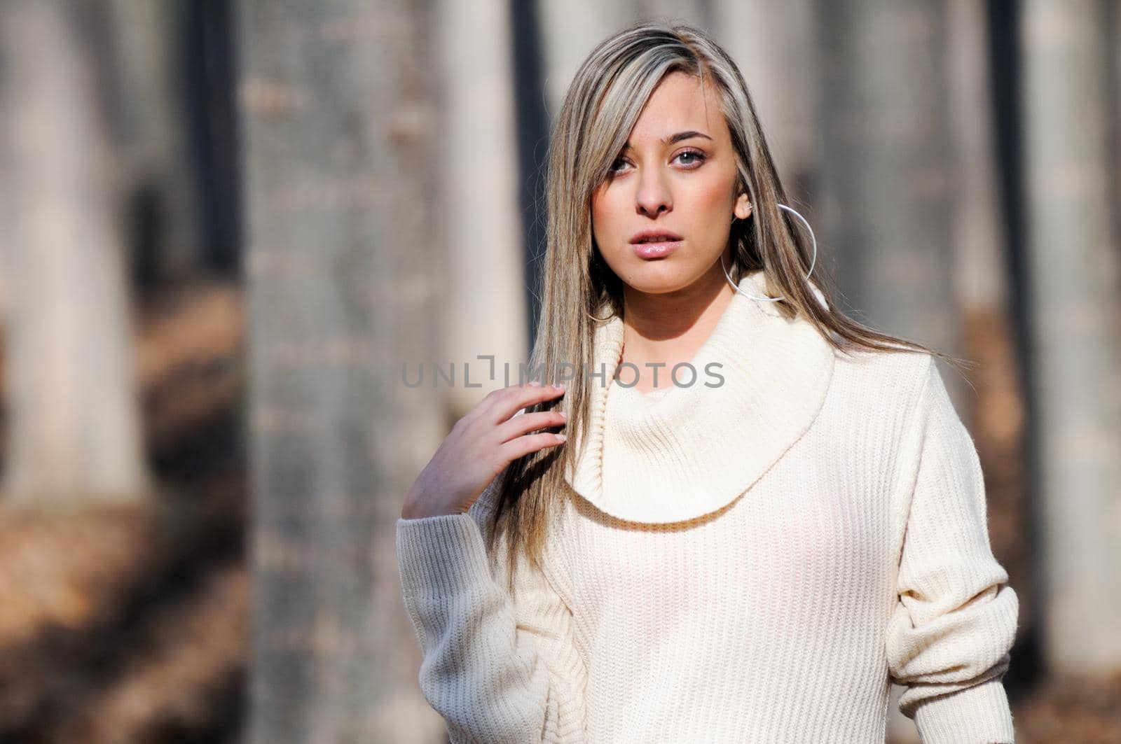 Beautiful blonde girl, dressed with a beige dress, standing in a poplar forest