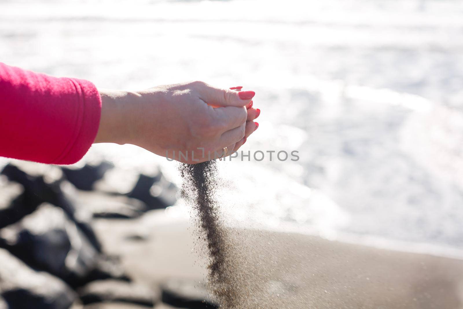 hand pours sand by the sea and rocks. symbol for time running out and time management. nails with manicure.