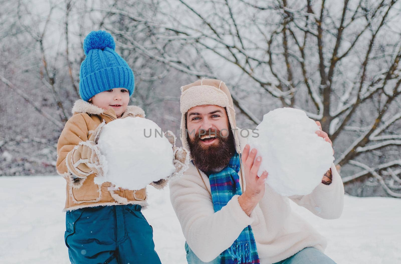 Winter, father and son play outdoor. Enjoying nature wintertime. Winter portrait of dad and child in snow Garden. Father and son making snowball on winter background. by Tverdokhlib