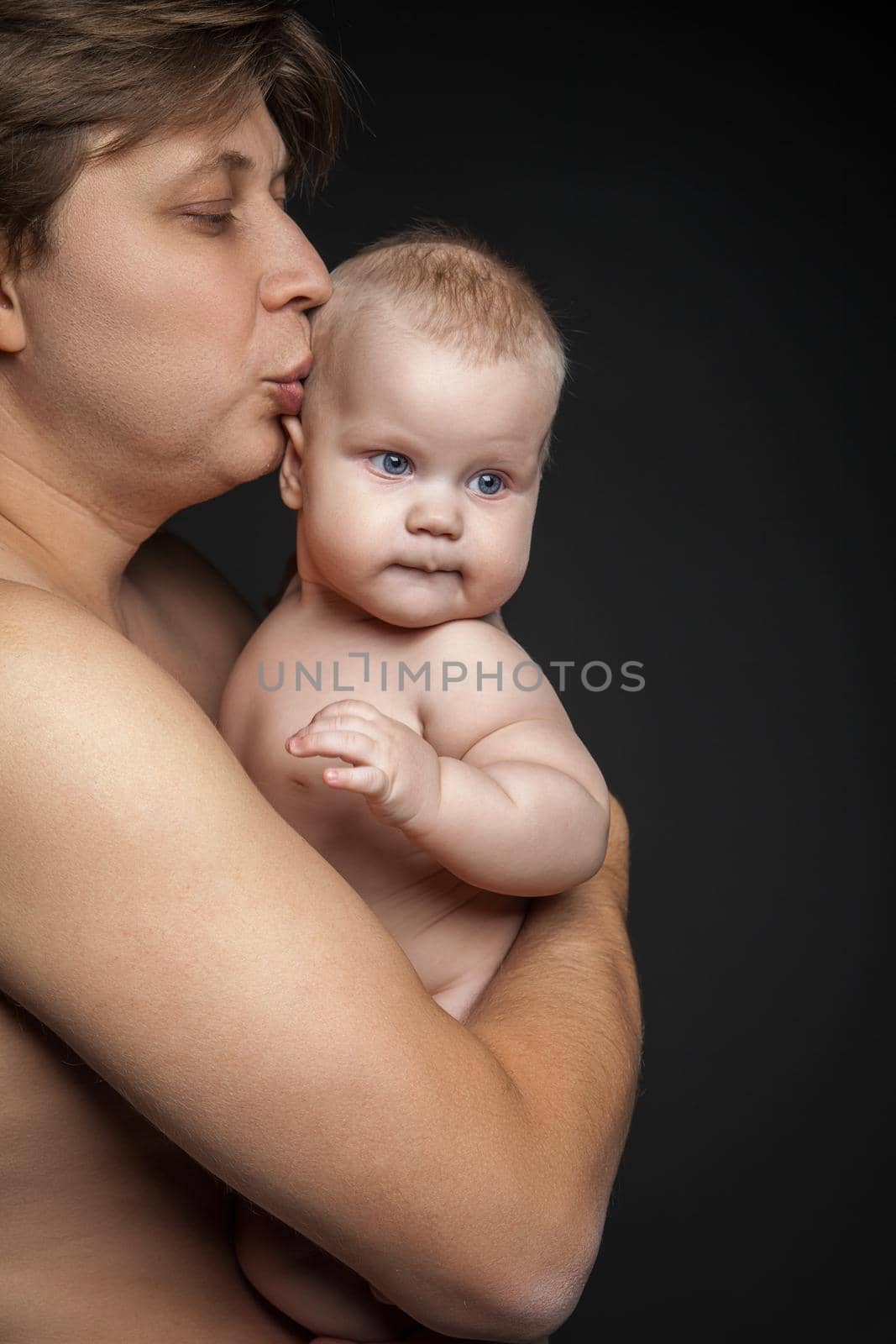 Happy father hugging and kissing his newborn baby. Focus on the child. Isolated over black background. Close up.
