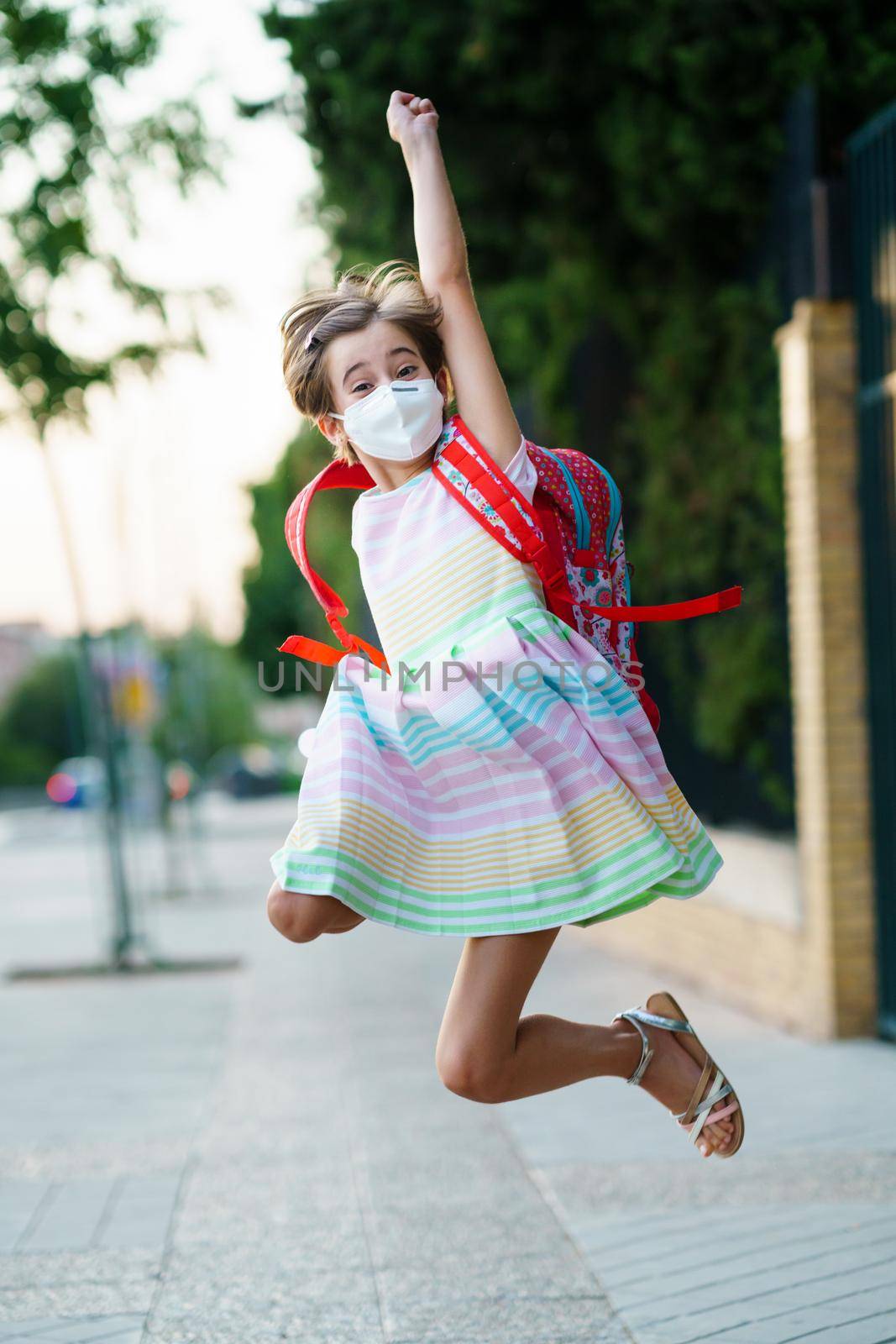 Girl wearing a mask takes a jump for joy at going back to school. by javiindy