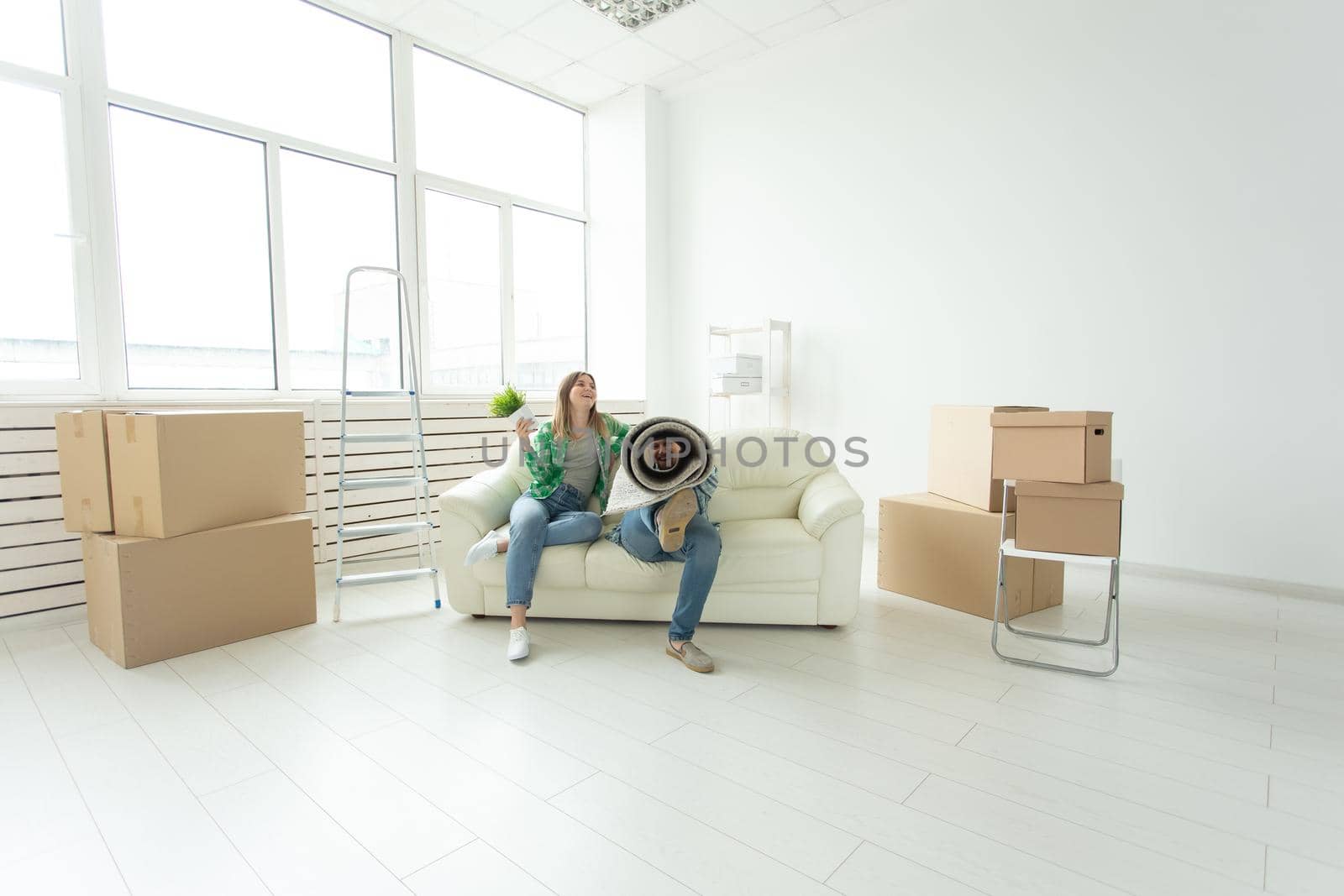 Cheerful joyful young couple charming girl and handsome man holding a box with things and a pot with a plant while moving to a new apartment. Housewarming and mortgage concept