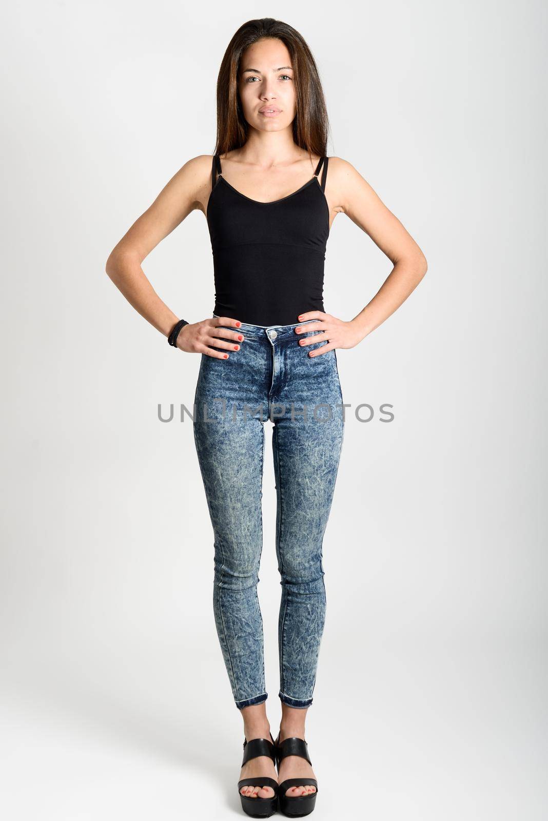 Young woman wearing black tank top and blue jeans on white background. Studio shot