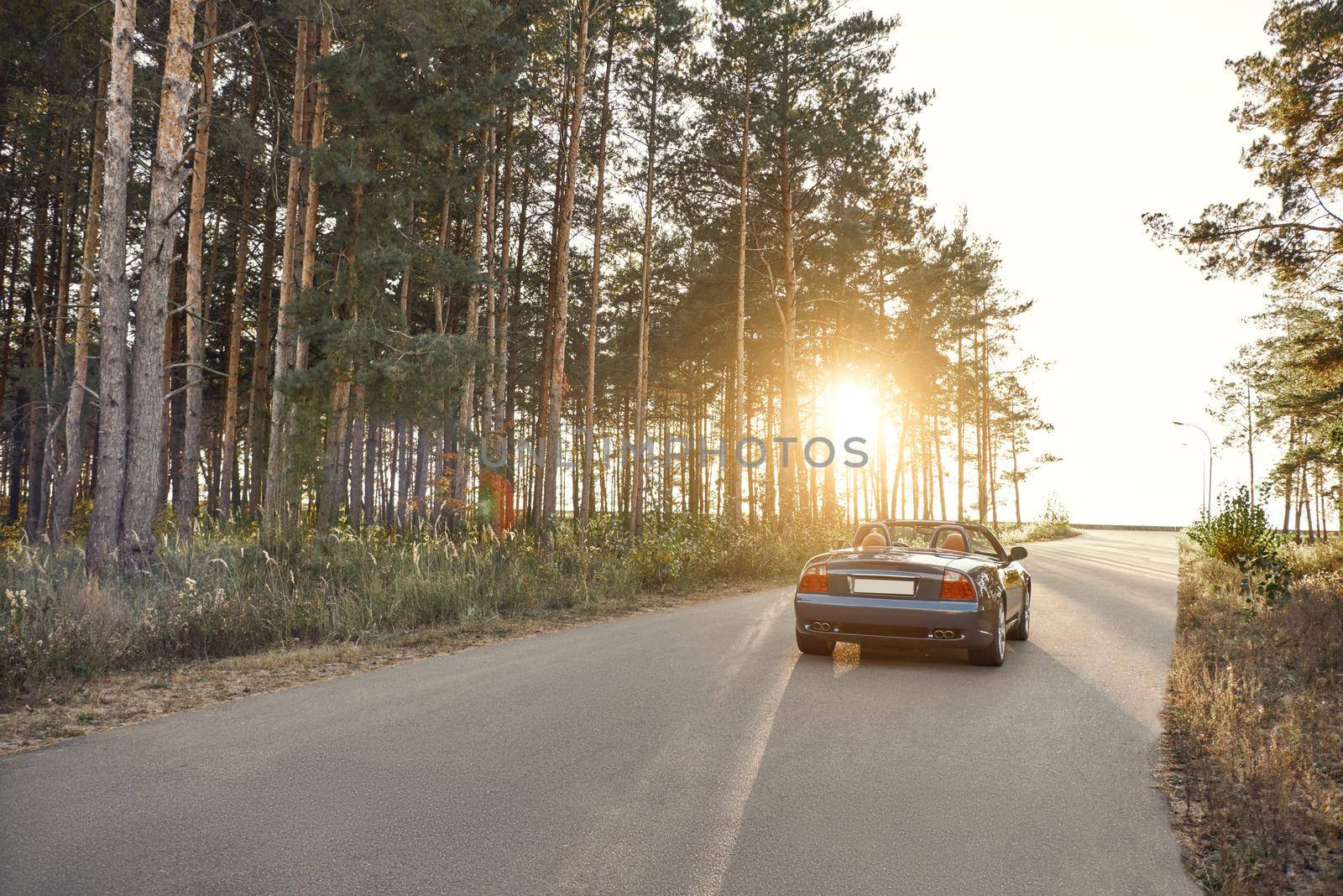 A black roofless car driving fast on the countryside asphalt road against morning sky with a beautiful sunrise