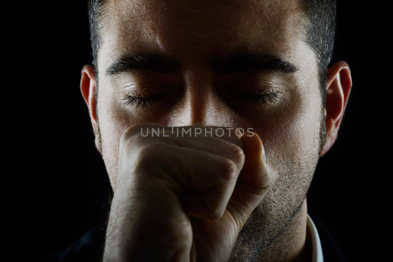 Portrait of a man with fist and eyes closed on black background