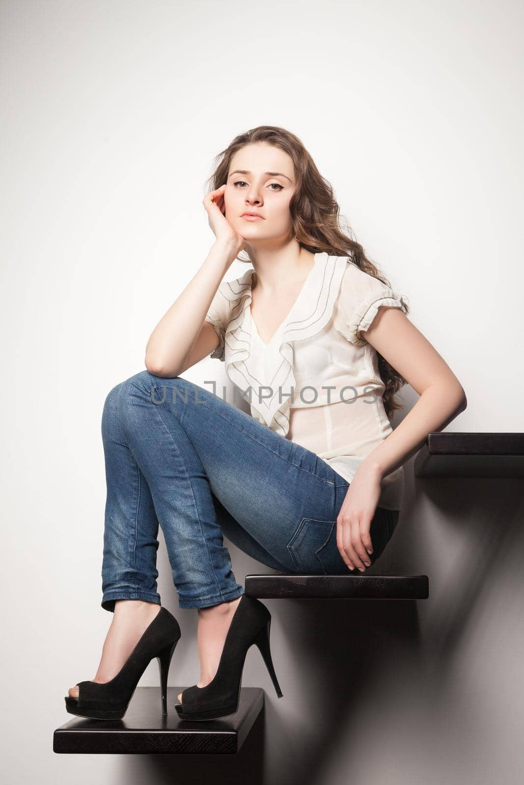 Portrait of beautiful stylish brunette with long hair looking at camera while sitting on steps