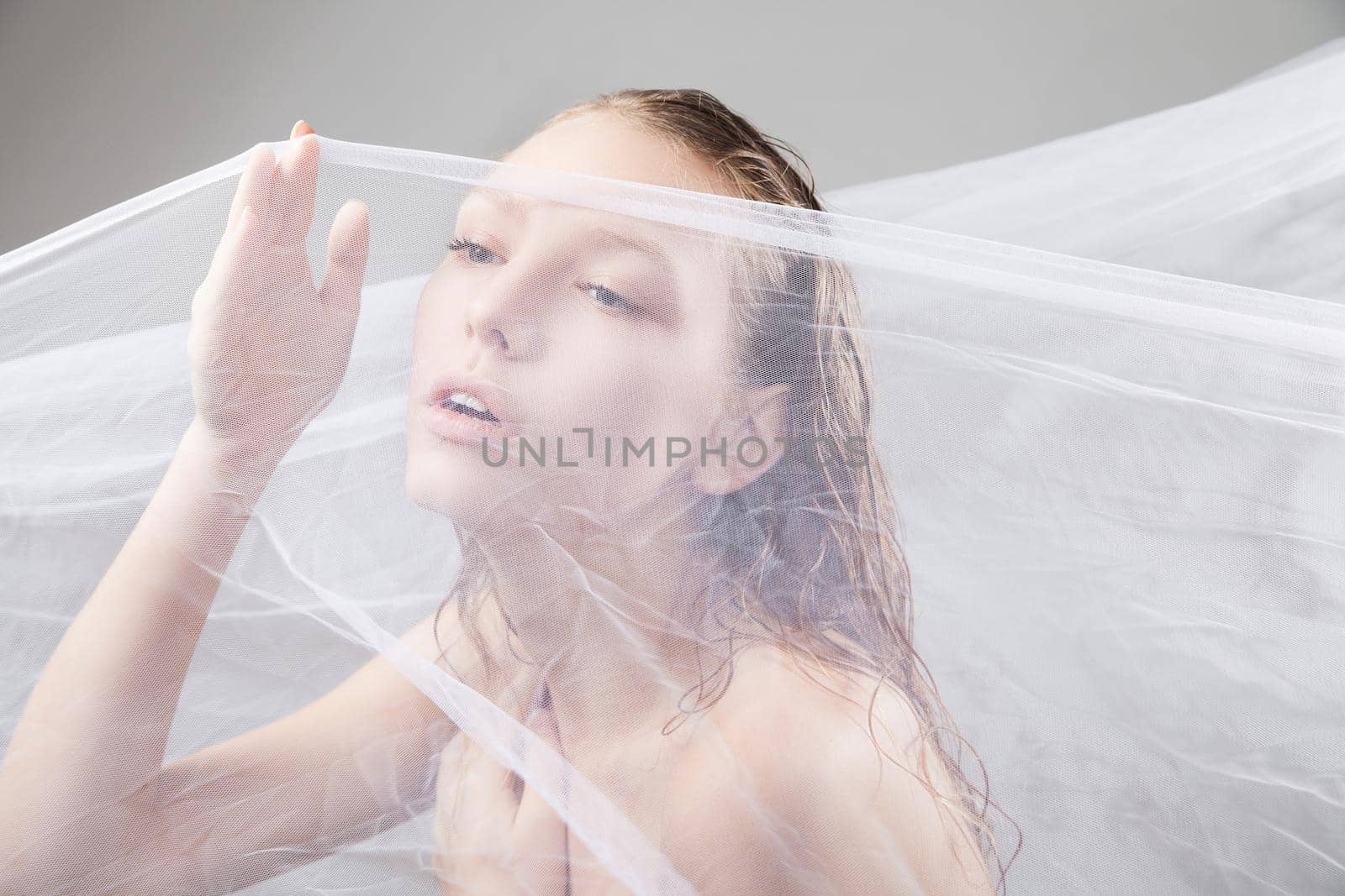 Close-up of beautiful wet woman face with waving fabric over light grey background