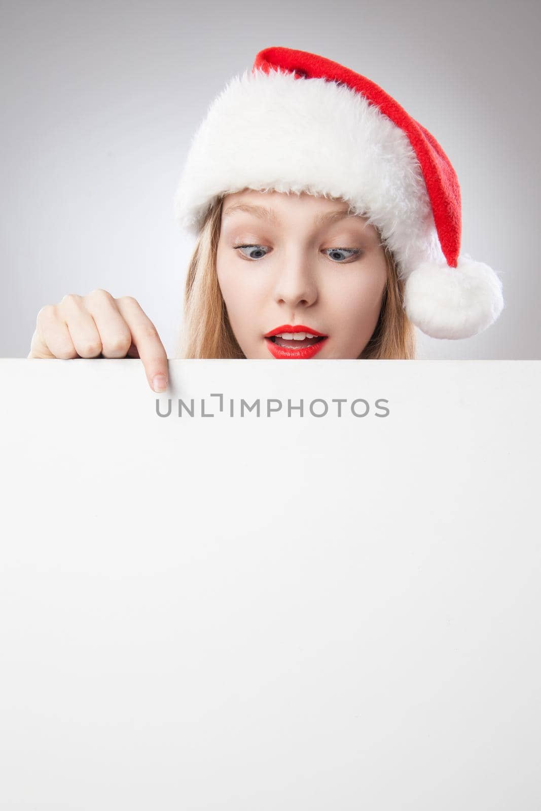 Beautiful christmas woman in santa hat pointing empty board, isolated on white background