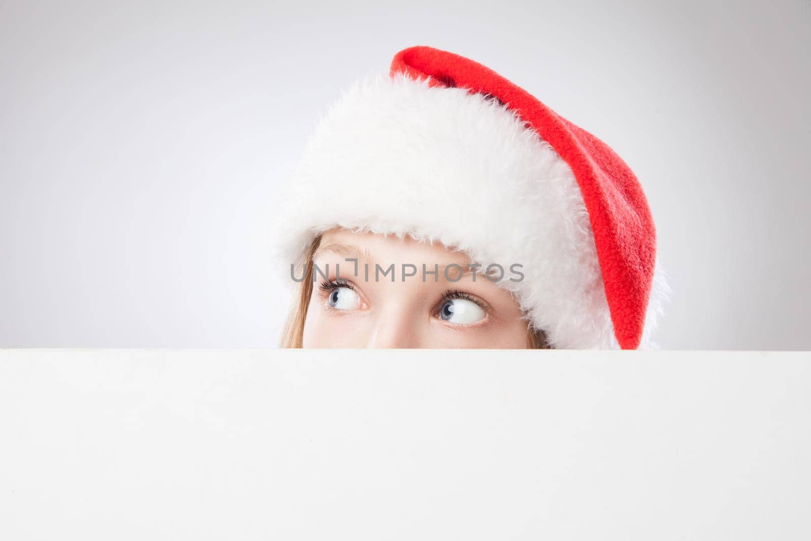 Beautiful christmas woman in santa hat holding empty board and looking to the left isolated on white background