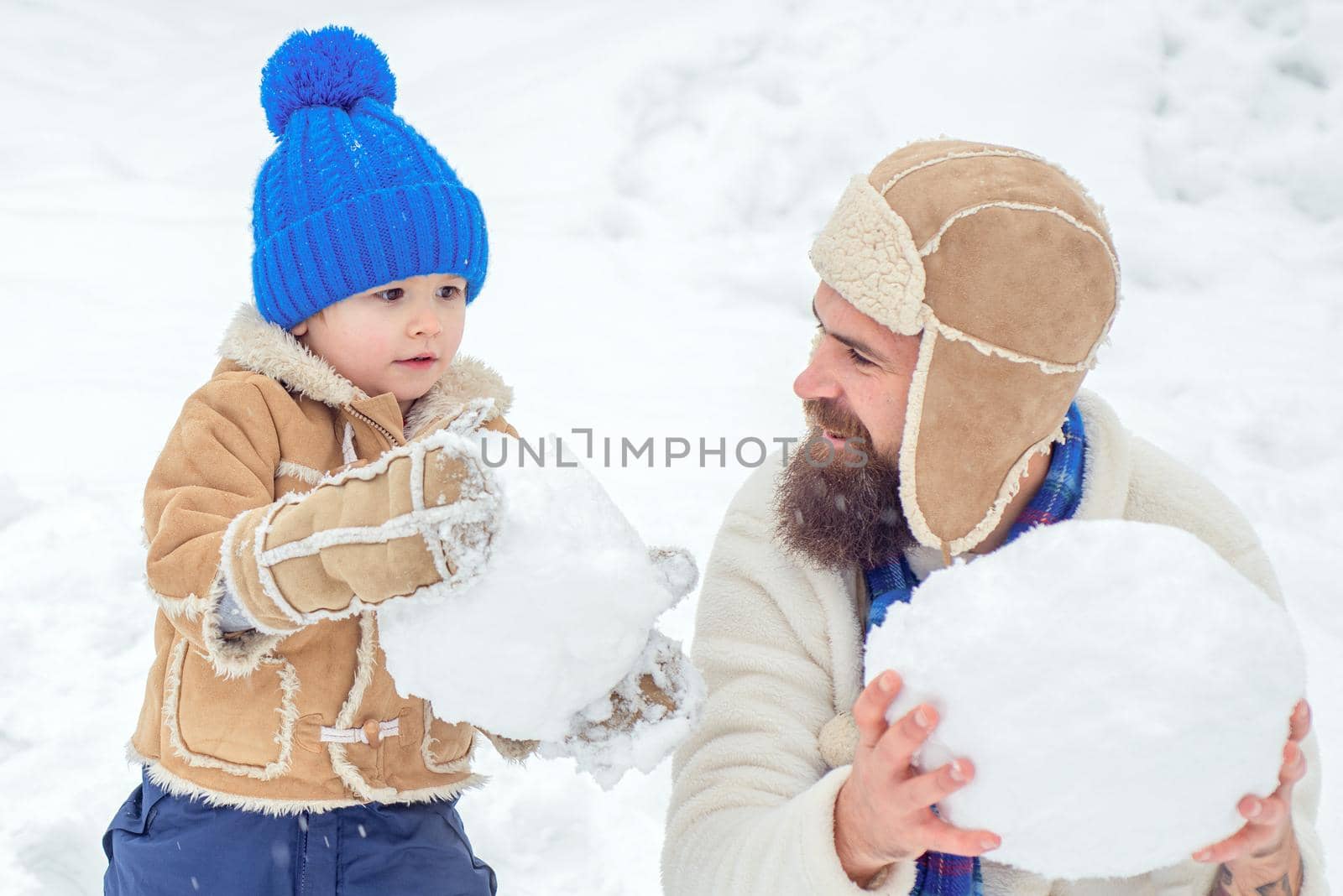 Winter, father and son play outdoor. Happy family plaing with a snow on a snowy winter walk. Father and son making snowball on winter background. by Tverdokhlib