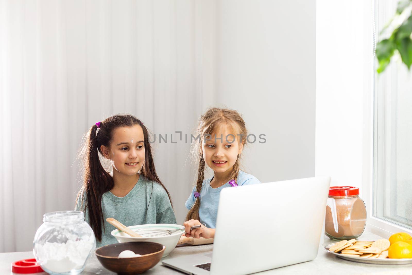 two girls learn to cook on a laptop online, watching video, smiling