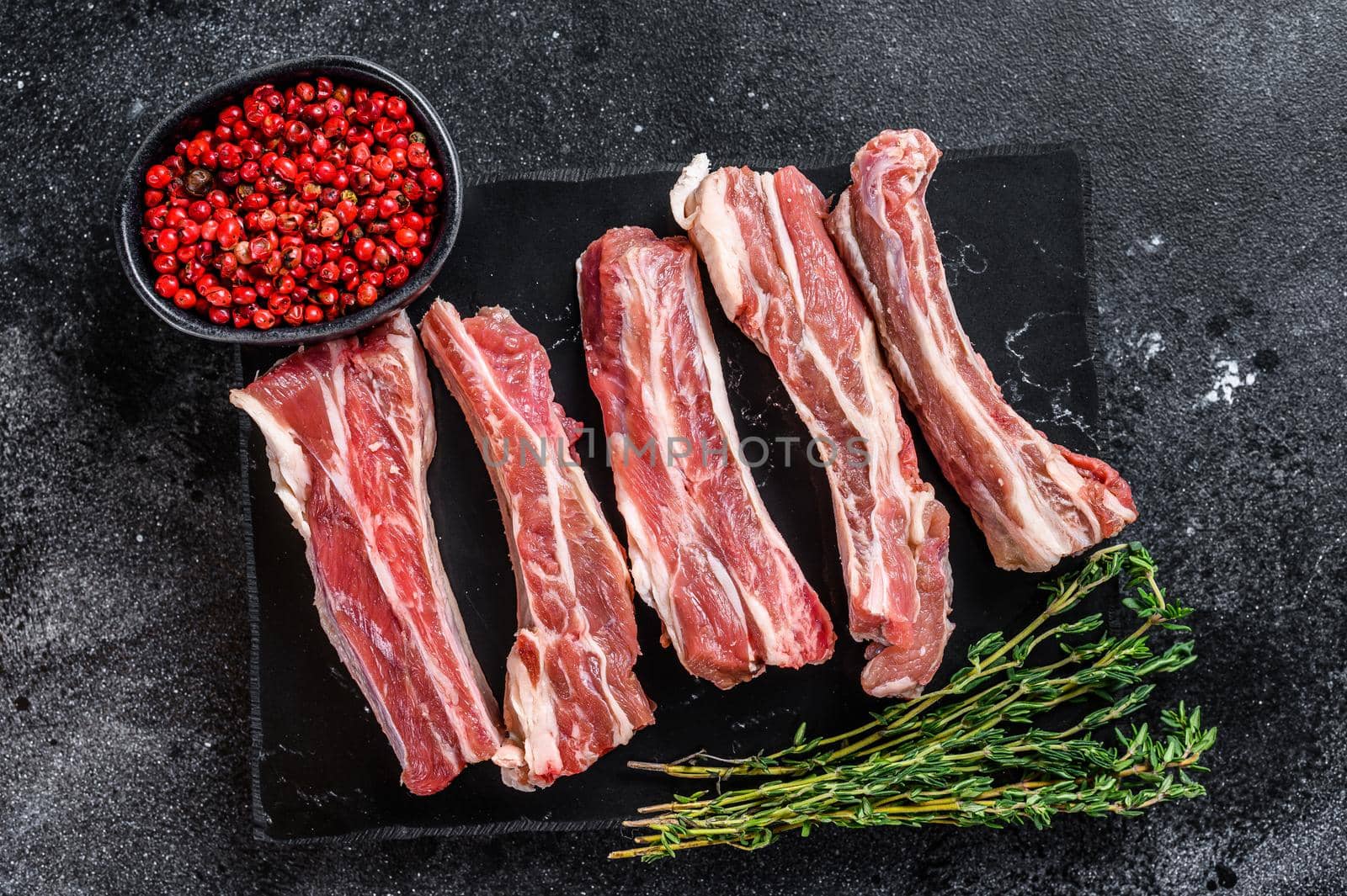 Raw sliced veal short spare loin ribs on a marble board. Black background. Top view. Copy space.