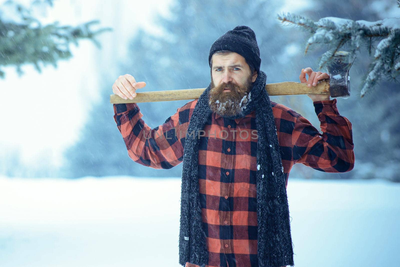 Hipster lumberjack man in snowy cold forest. Winter man with beard hold axe. by Tverdokhlib