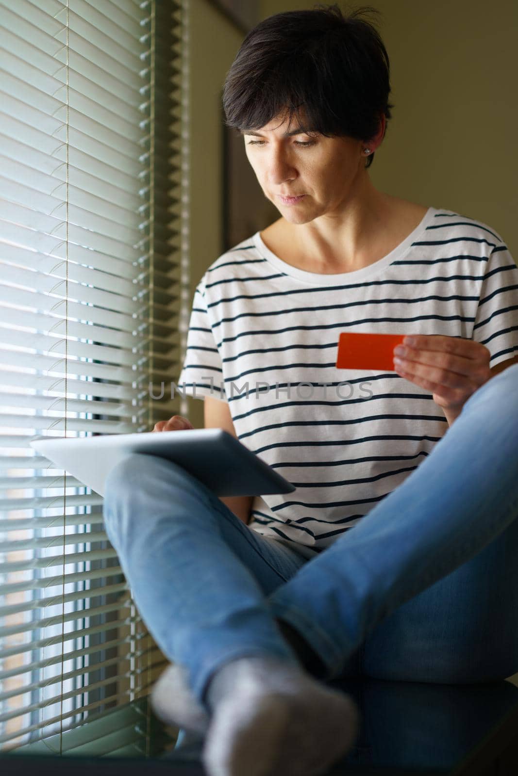 Middle-aged woman shopping online with her digital tablet paying with a credit card. Female in her 50s