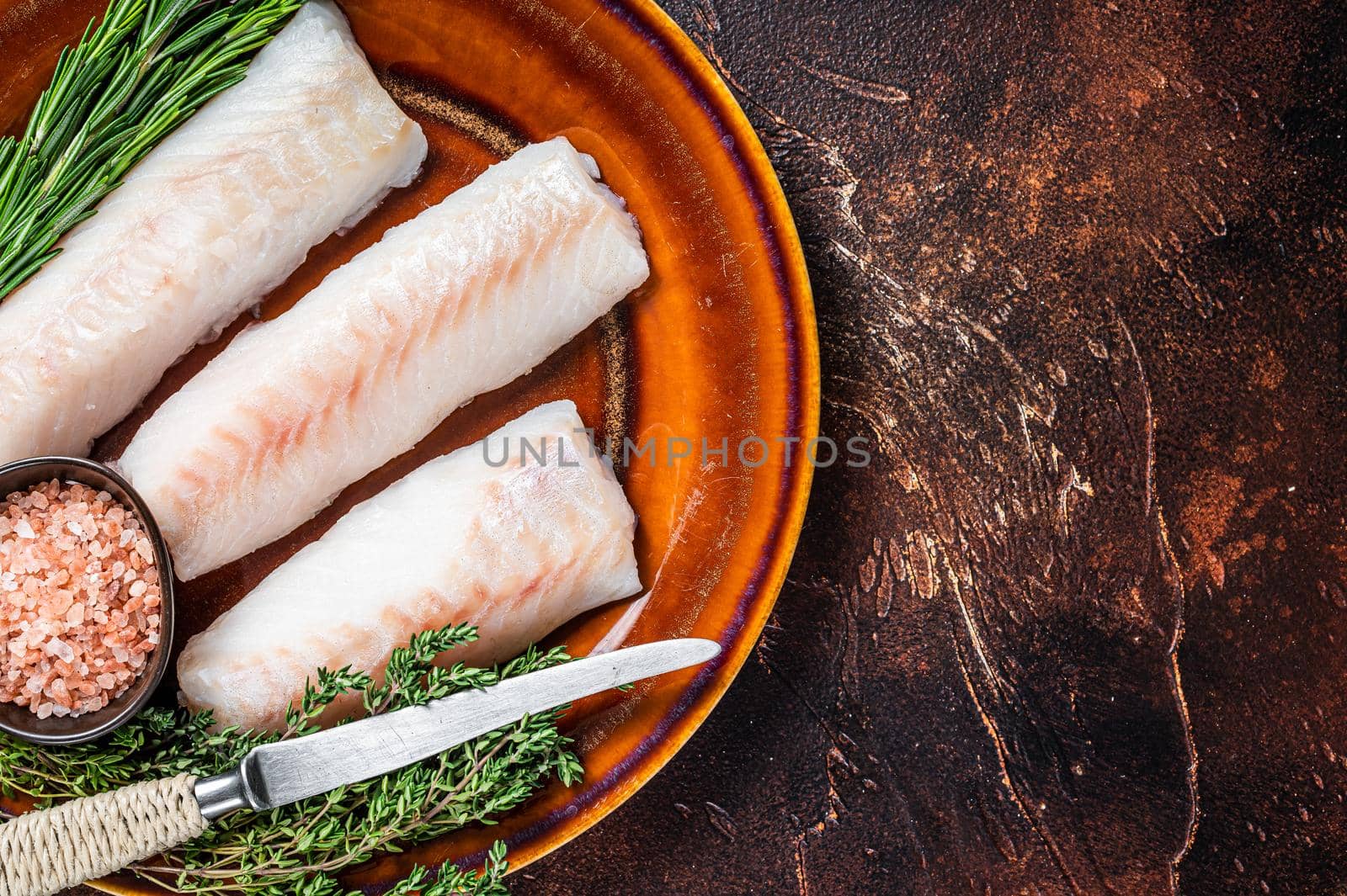 Raw cod loin fillet steaks on rustic plate with thyme and salt. Dark background. Top view. Copy space by Composter