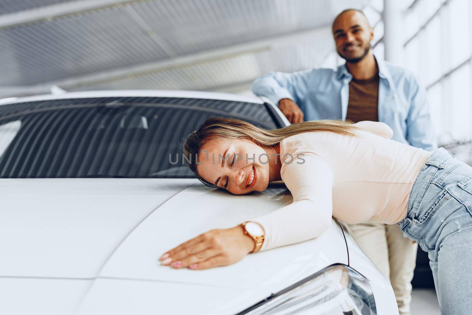 Young couple man and woman hugging their new car in a car shop close up