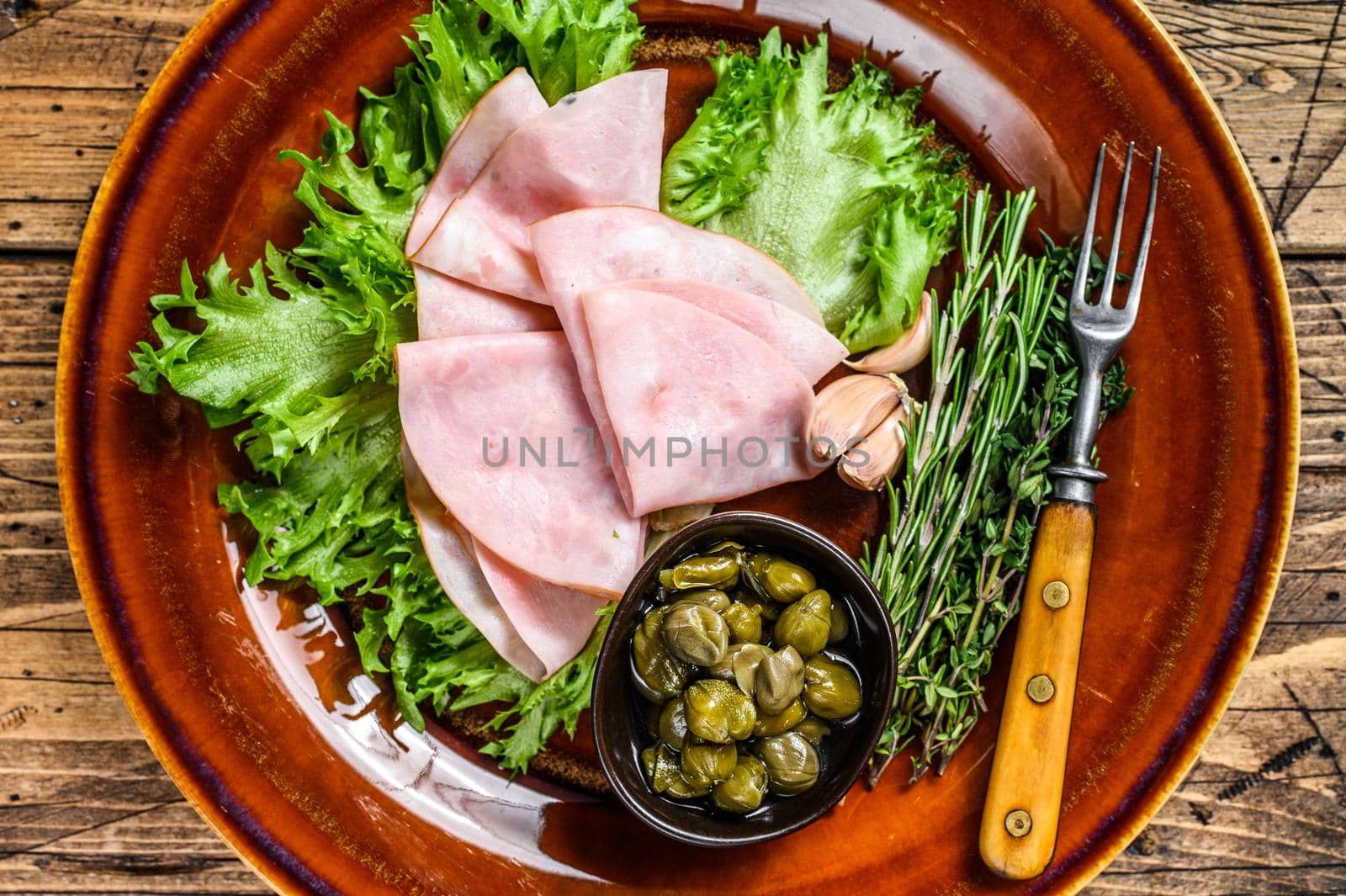 Sliced smoked ham with fresh salad and capers on a plate. wooden background. Top view.
