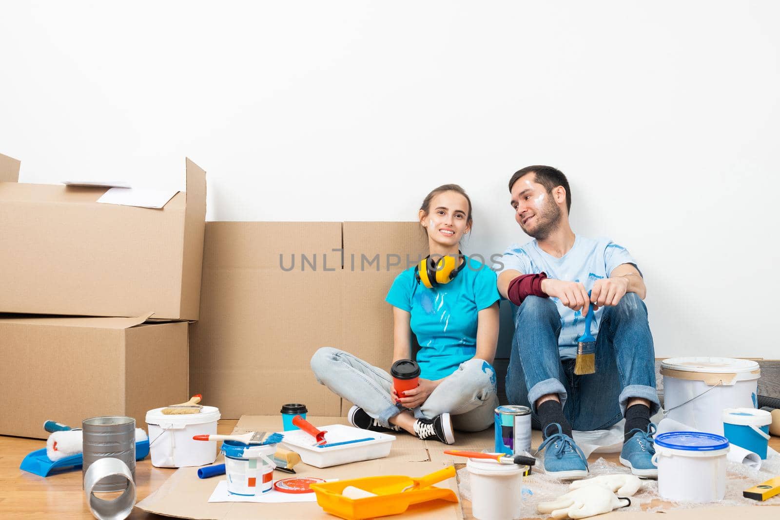 Happy couple together sitting on floor among cardboard boxes. Young man and woman relaxing after moving in their new house. House remodeling and interior renovation. Families moving concept.