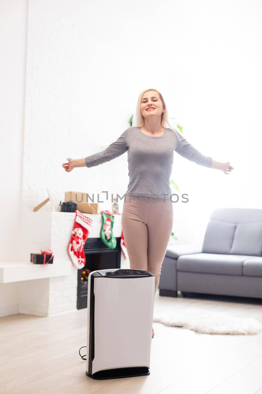 Air purifier in a living room, woman working with laptop with filter for clean room by Andelov13